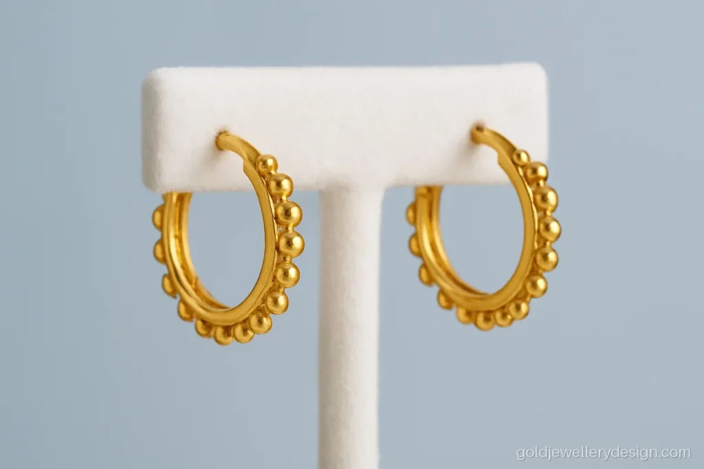 Simple gold baliya design with small beads in a huggie style on an earring stand