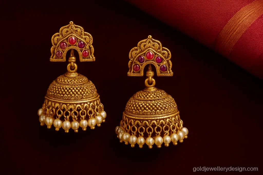 Bridal gold jhumka design with temple arch stud, ruby drops and pearl fringe