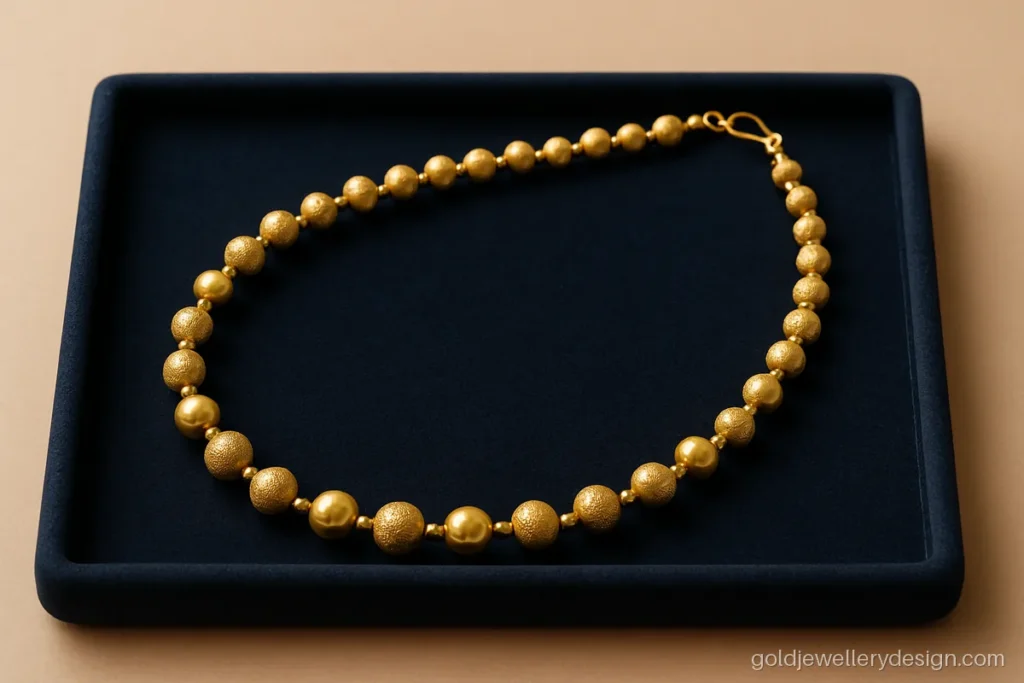Simple gold necklace design with alternating plain and textured gold balls on a velvet tray