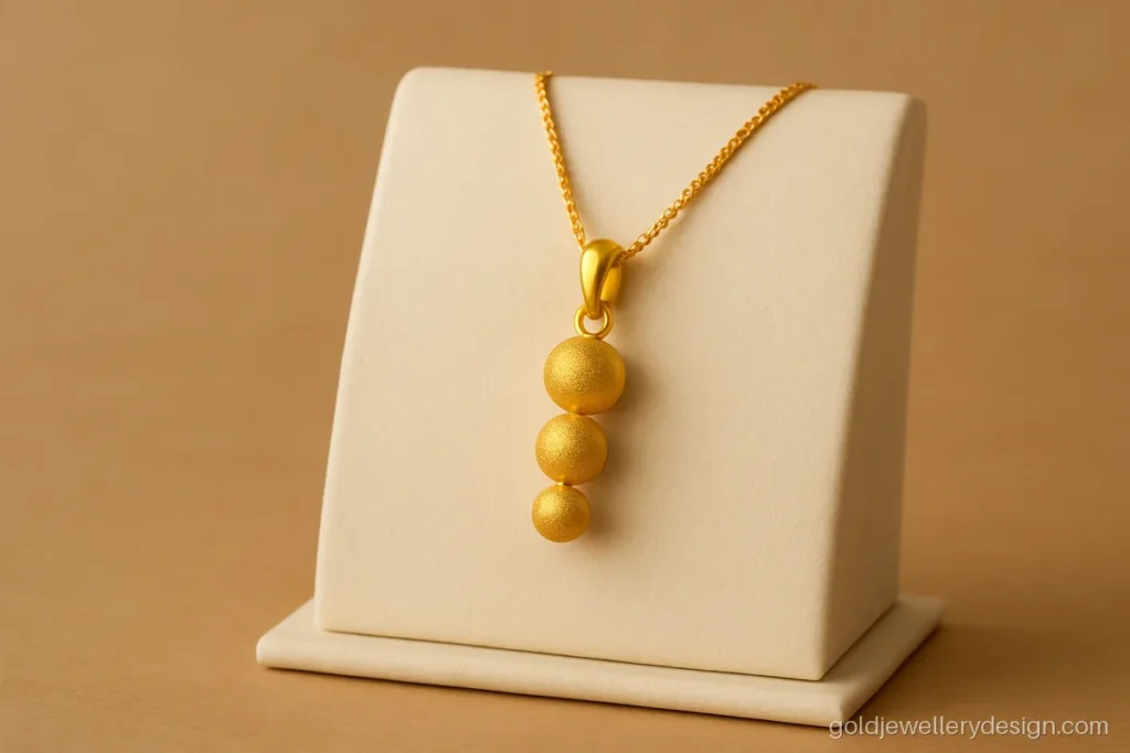 Light gold pendant with three small textured gold balls in a vertical drop