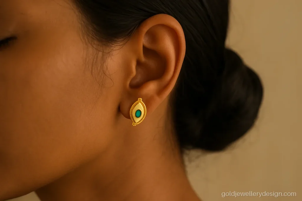 Gold kammal design with a small mango shape and green stone worn on the ear