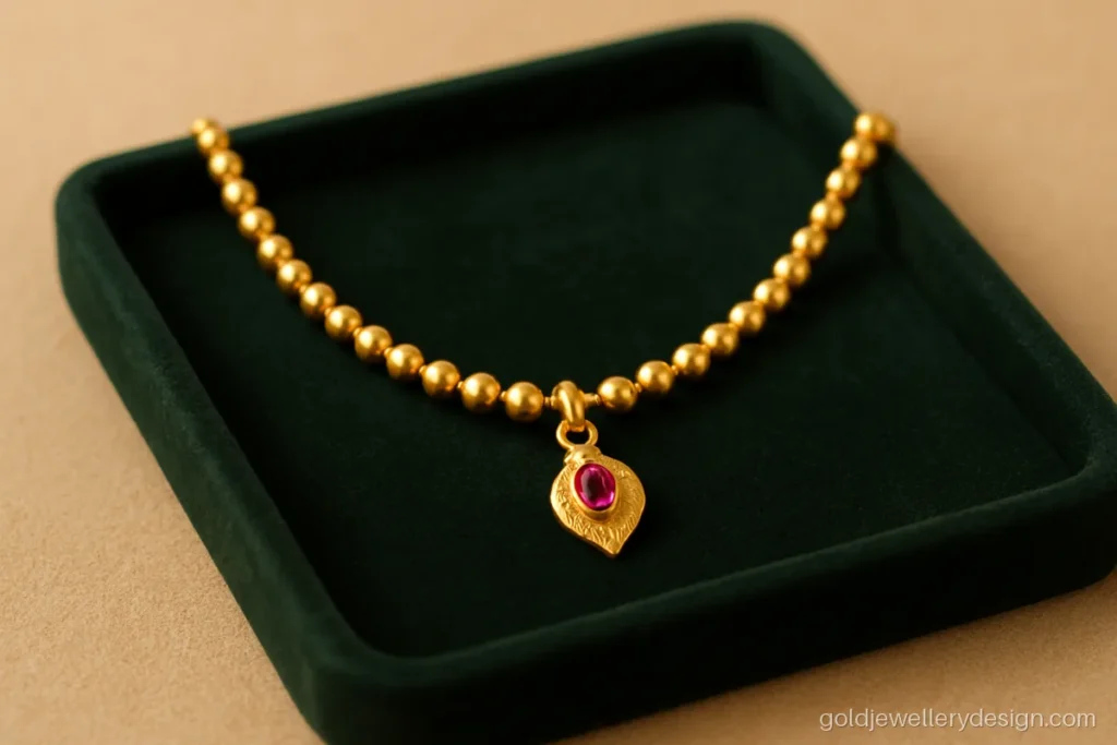Short kanthi design gold necklace with round beads and a small ruby pendant on a tray